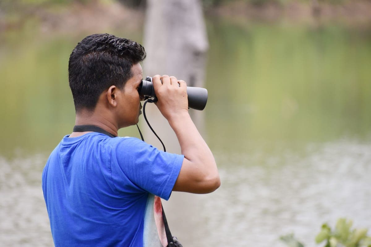 A man using binoculars beside a lake